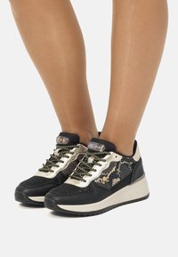 Sneaker in pelle di serpente nera e dorata con pannelli in rete, superfici testurizzate, dettagli metallici e una suola bianca imbottita; design con lacci.