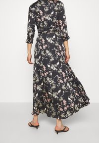 Dlouhé černé šaty s květinovým potiskem a ptáky, s třičtvrtečními rukávy, vypasovaným pasem a splývavou sukní.