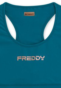 Sujeta de deporte en color teal, fabricada con un material suave, con un escote redondeado y un diseño de espalda nadadora, que presenta un logo en color oro rosa "FREDDY" en la parte delantera.