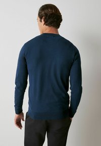 Pull bleu marine à manches longues et col rond. Matière en maille douce avec une coupe ajustée et poignets et bordures côtelés. Texture lisse.