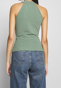 Top halter de canalé en verde oliva con una silueta ajustada y cuello alto, combinado con pantalones de mezclilla azul de tiro alto.