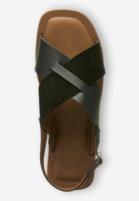 Sandale en cuir noir et suède vert avec un design à bretelles croisées, semelle intérieure marron et boucle ajustable à la cheville.