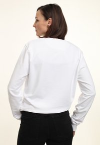 Felpa bianca a maniche lunghe in cotone, con scollatura rotonda e vestibilità morbida, abbinata a jeans neri. Design semplice, senza loghi visibili.