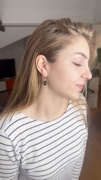 Øredobber i gulltoner med en tårnedråpeformet svart edelsten, som har en teksturert innfatning, båret av en person med langt, rett hår.