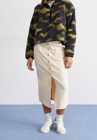 Polarowy polar w desenie moro w odcieniach zieleni i szarości. Wysoki kołnierz, zamek na pół, zestawiony z beżową spódnicą zapinaną na guziki.