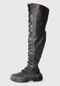 Bottine en cuir noir montante avec lacets, semelle épaisse et détails de surpiqûres jaunes.