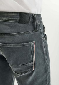 Jeans in denim grigio con una patch in pelle in vita, una tasca laterale con cuciture a contrasto e un taglio pulito e moderno.