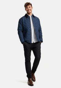 Navy quilted jacket with a collar, black pants, and brown leather boots. Features button closure and side pockets. Structured design.