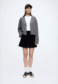 Szary krótki kardigan ze złotymi guzikami, biała koszulka, czarna spódnica ze sztruksu, czarne trampki z białymi i beżowymi akcentami oraz białe skarpetki.