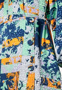 Vestido multicolorido com um design de patchwork em tons de azul-marinho, verde, laranja e roxo, tecido texturizado e botões decorativos.