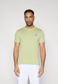 Ανοιχτό πράσινο βαμβακερό μπλουζάκι με στρογγυλή λαιμόκοψη και κοντά μανίκια. Διαθέτει μικρό σκοτεινό λογότυπο Lacoste στο στήθος. Ομαλή υφή.