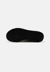 Svart gummisula med aggressivt mönster; har varierande texturer för grepp och stabilitet; designad för utomhusaktiviteter.