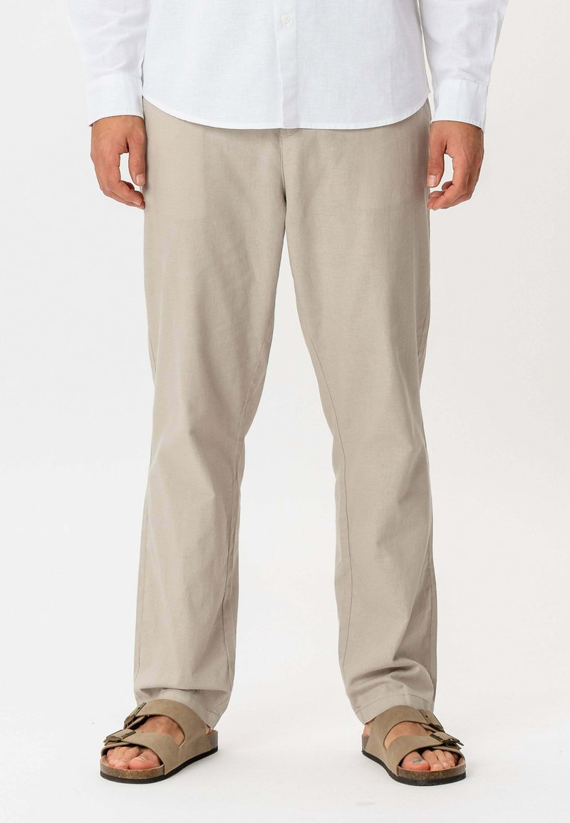 Pantalon en lin beige avec une coupe droite, doté d'une texture légère et de rides minimales, associé à des sandales marron.
