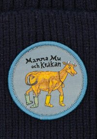 Marineblå ribbad tyg med en rund broderad patch som har en gul ko med gröna stövlar, märkt "Mamma Mu och Kykán" i svart text.