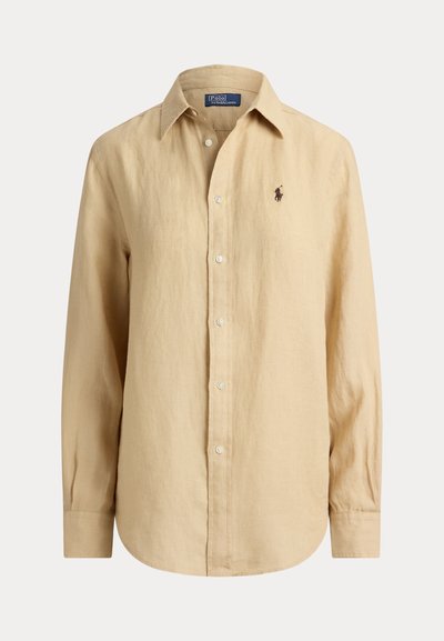 Chemise beige à manches longues avec boutons, col, petit logo brodé sur le côté gauche de la poitrine et boutons visibles sur le devant.