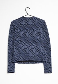 Veste à manches longues avec motif pixélisé bleu et noir suspendue sur un cintre noir sur fond blanc.