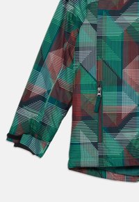 Manica di giacca colorata con motivo geometrico in verde, rosso, bianco e nero, dotata di tasca con zip e polsino regolabile in Velcro.