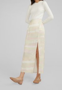 Kvinna klädd i en pastellfärgad tie-dye midi-skjorta med hög slits, vit ribbad långärmad topp och beige vävd slingback-sandal.