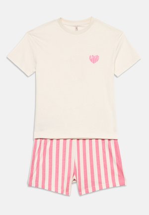 Cremefarbenes T-Shirt mit kurzen Ärmeln und rosa Herzlogo auf der Brust, kombiniert mit rosa-weiß gestreiften Shorts mit verticalen Streifen.