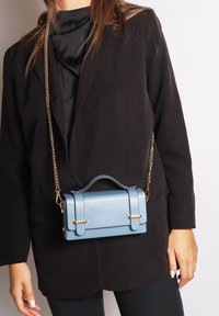 Borsa in finta pelle blu chiaro con un design strutturato, manico superiore e hardware color oro. Dotata di una tracolla a catena rimovibile.
