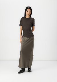 Top corto a maniche corte marrone scuro con arricciature laterali, abbinato a una lunga gonna in satin verde oliva. Stivali neri con tacco completano l'outfit.