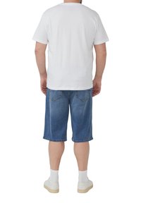 Biała koszulka z krótkim rękawem połączona z niebieskimi szortami dżinsowymi do połowy uda. Białe sneakersy i skarpetki do kostek dopełniają strój.