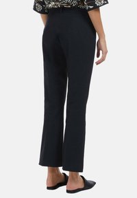 Pantalons tailleur marine avec une coupe droite, dotés d'une taille mi-haute et de plis marqués, associés à des chaussures noires à enfiler.