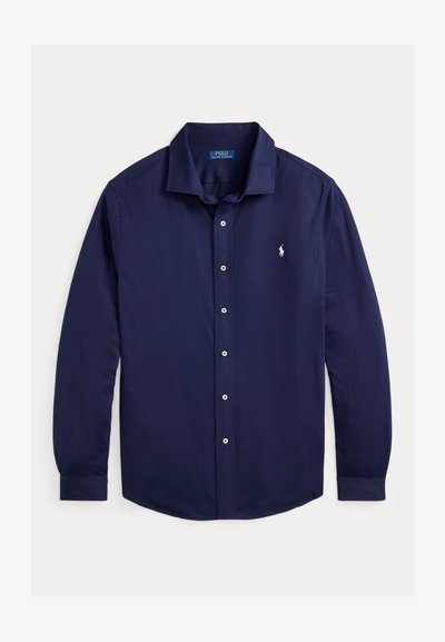 Ναυτικό μπλε πουκάμισο μακρύ μανίκι από βαμβάκι, με κολάρο που κλείνει με κουμπί, εμπρόσθια κουμπότρυπα και ένα μικρό κεντητό λογότυπο στο στήθος.