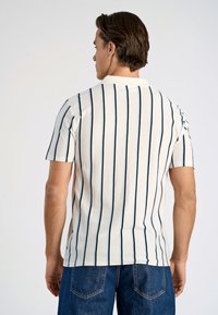 Kortärmad pikétröja med vertikala blåa och marinblå ränder på en kr�ämfärgad bakgrund. Tyget ser slätt ut; kragen är klassisk och strukturerad.