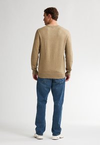 Beige gebreide trui met een ronde hals, geribbelde manchetten en onderrand, gecombineerd met losse blauwe spijkerbroeken. Witte sneakers maken de look compleet.