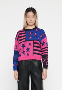 Genser i rosa, blå og svart strikk med stjerne- og stripemønster. Løs passform, rund halslinje og ribbestrikkede mansjetter og nederkant.