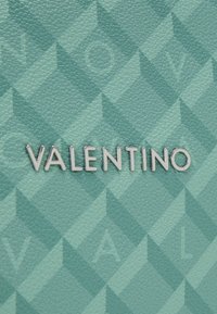 Aquamarintexturerat läder med diamantmönster; silverfärgad "VALENTINO"-logotyp som är tydligt synlig och reflekterar ljus.