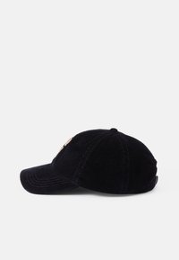 Svart kordfløyelsbaseballcaps med rund krone, buet skygge og brodert logodetalj på forsiden. Teksturert stoff er synlig.