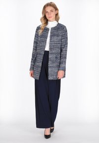 Marineblauwe en witte textuurjack met een ronde halslijn, voorkennis, en een open voorkant ontwerp, gecombineerd met marineblauwe wijde broek en zwarte schoenen.