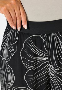 Zwarte rok met een brede elastische tailleband en grote witte bloemenpatronen. Gladde textuur met verticale lijnen die het ontwerp accentueren.