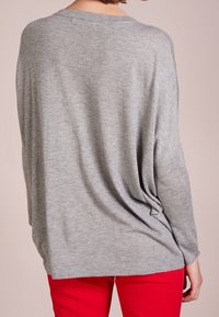 Hellgrauer, übergroßer Pullover mit fallenden Schultern und weicher Textur, der eine entspannte Passform aufweist und sich locker um die Taille legt.