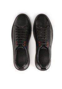 Sneakers in pelle nera con una texture liscia, dotati di occhielli rossi e una chiusura con lacci. Suola in gomma spessa per una maggiore durata.