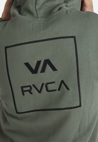 Green hoodie made of soft fabric features a black rectangular graphic with "VA" and "RVCA" logos prominently displayed on the back.