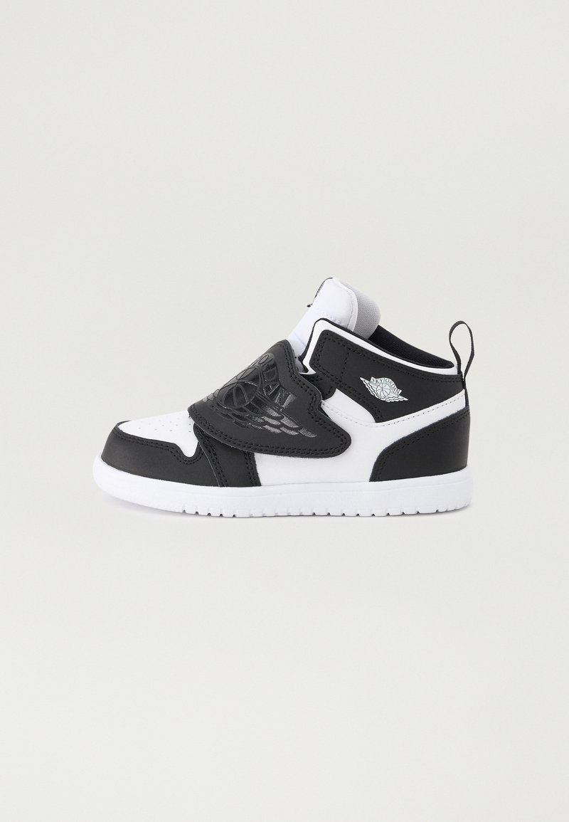 Crne i bijele tenisice s glatkim kožnim gornjim dijelom, podstavljenim ovratnikom, podesivim remenom i bijelim gumeni đonom. Imaju logotip kao dodatak.