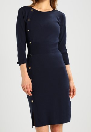 Navyblauwe jurk tot op de knie met driekwartmouwen, met een rij gouden knopen langs de zijkant en een kleine zijsplit.