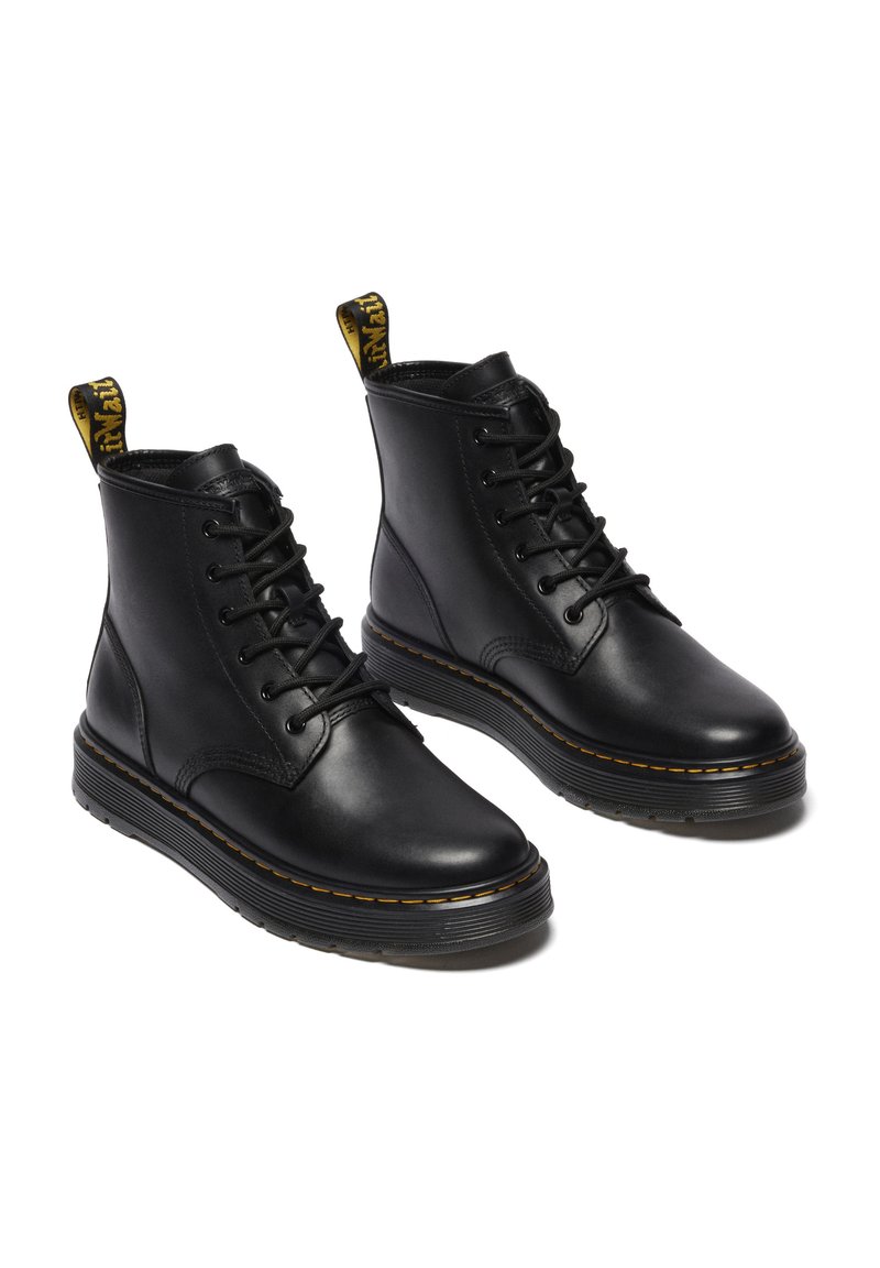 Bottines en cuir noir avec un bout arrondi, fermeture à lacets à l'avant et une languette jaune. Elles présentent une semelle en caoutchouc épaisse avec des coutures visibles.
