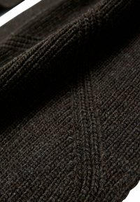 Tessuto lavorato a maglia marrone scuro con un motivo testurizzato e costine diagonali. Il materiale appare morbido e denso, con una superficie leggermente pelosa.