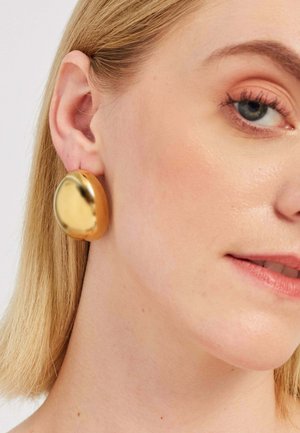 Zlate okrogle uhane iz kovine z polirano, odsevnimi površinami, ki prikazujejo gladke krivulje in trden, močan dizajn.