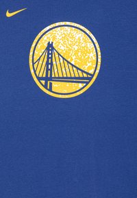 Camiseta de algodón azul con un gráfico amarillo de un puente dentro de un diseño circular, con un fondo texturizado y el logo de Nike en la parte superior.