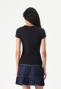 Zwart T-shirt met korte mouwen, een aansluitend ontwerp, ronde hals en een gladde textuur. Gecombineerd met een spijkerrok met ruches in donkerblauw.