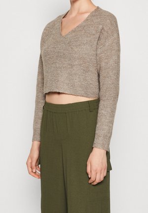 Personne portant un pull en maille beige court à manches longues et un pantalon vert olive taille haute avec poches latérales.