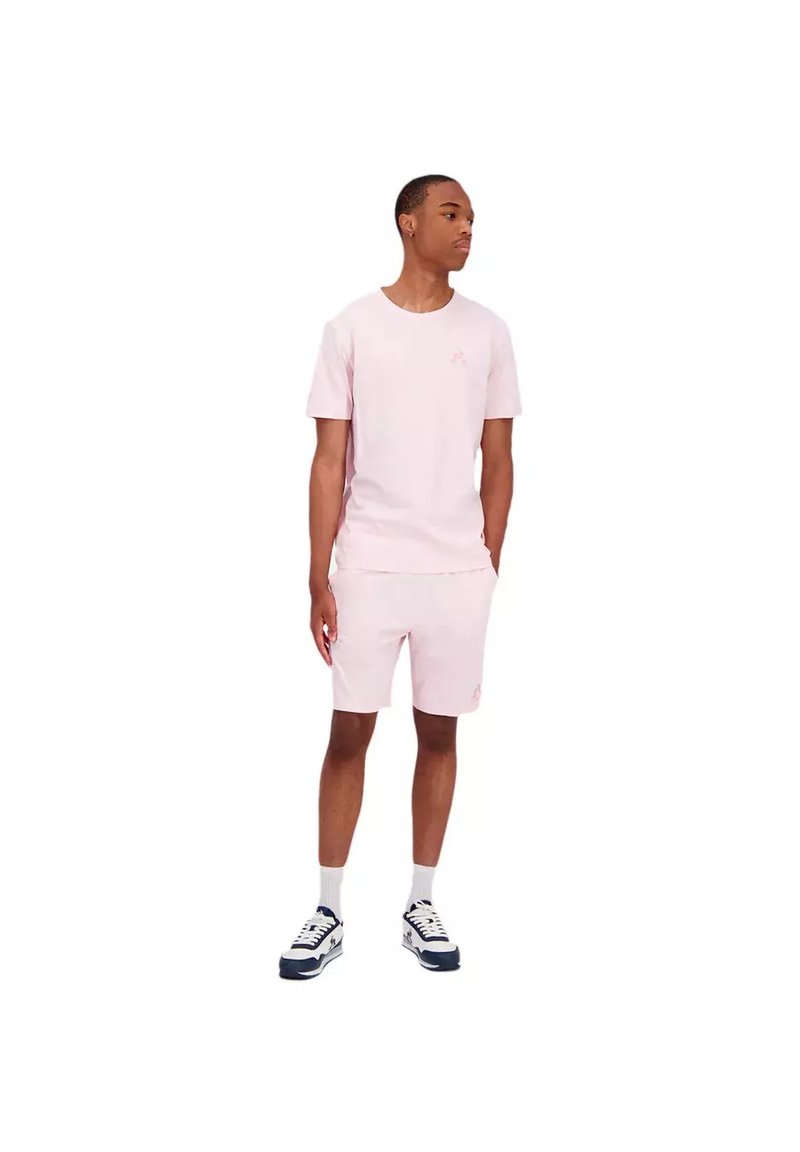 Ensemble en coton rose clair composé d'un t-shirt et d'un short assorti. Il présente des manches courtes, un col rond et un logo brodé sur la poitrine.