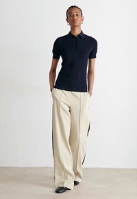 Polo shirt navy a maniche corte con un design testurizzato, abbinato a pantaloni a gamba larga beige chiaro con strisce laterali nere.