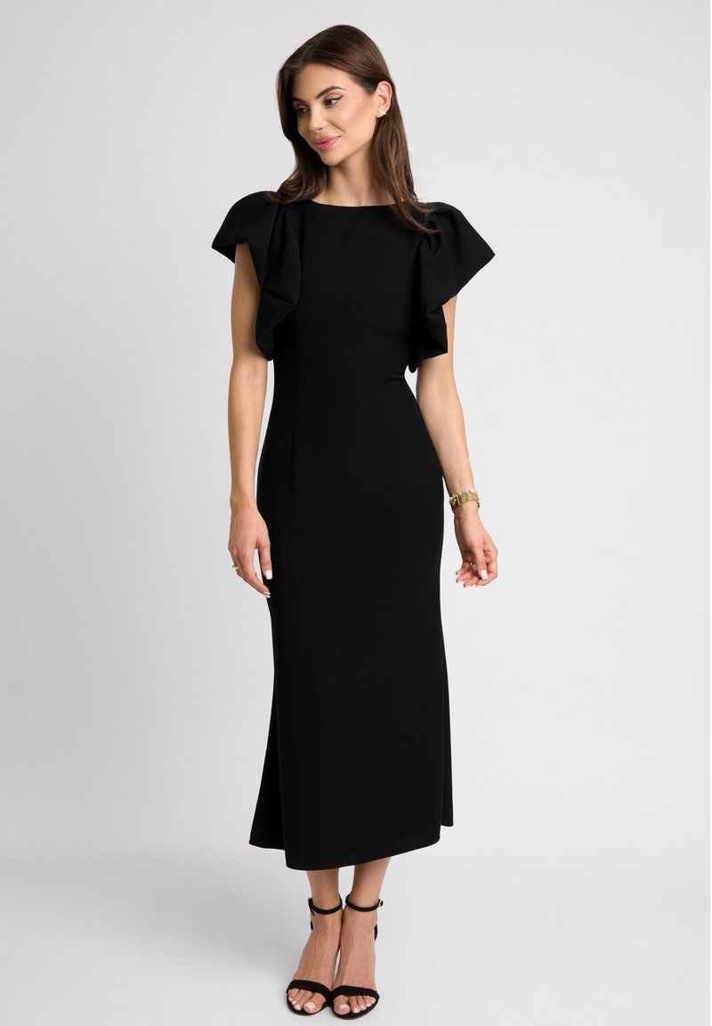 Czarna midi sukienka z krótkimi falbaniastymi rękawami, dopasowaną górą i rozkloszowanym dołem. Gładka faktura; w zestawieniu z czarnymi sandałami na obcasie.