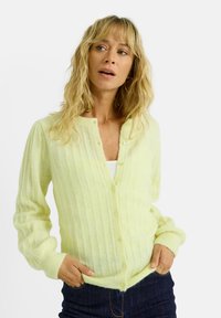 Cardigan de color amarillo claro con relieve, hecho de material suave, con un escote redondo, cierre de botones y mangas largas. Diseño simple sin patrones.